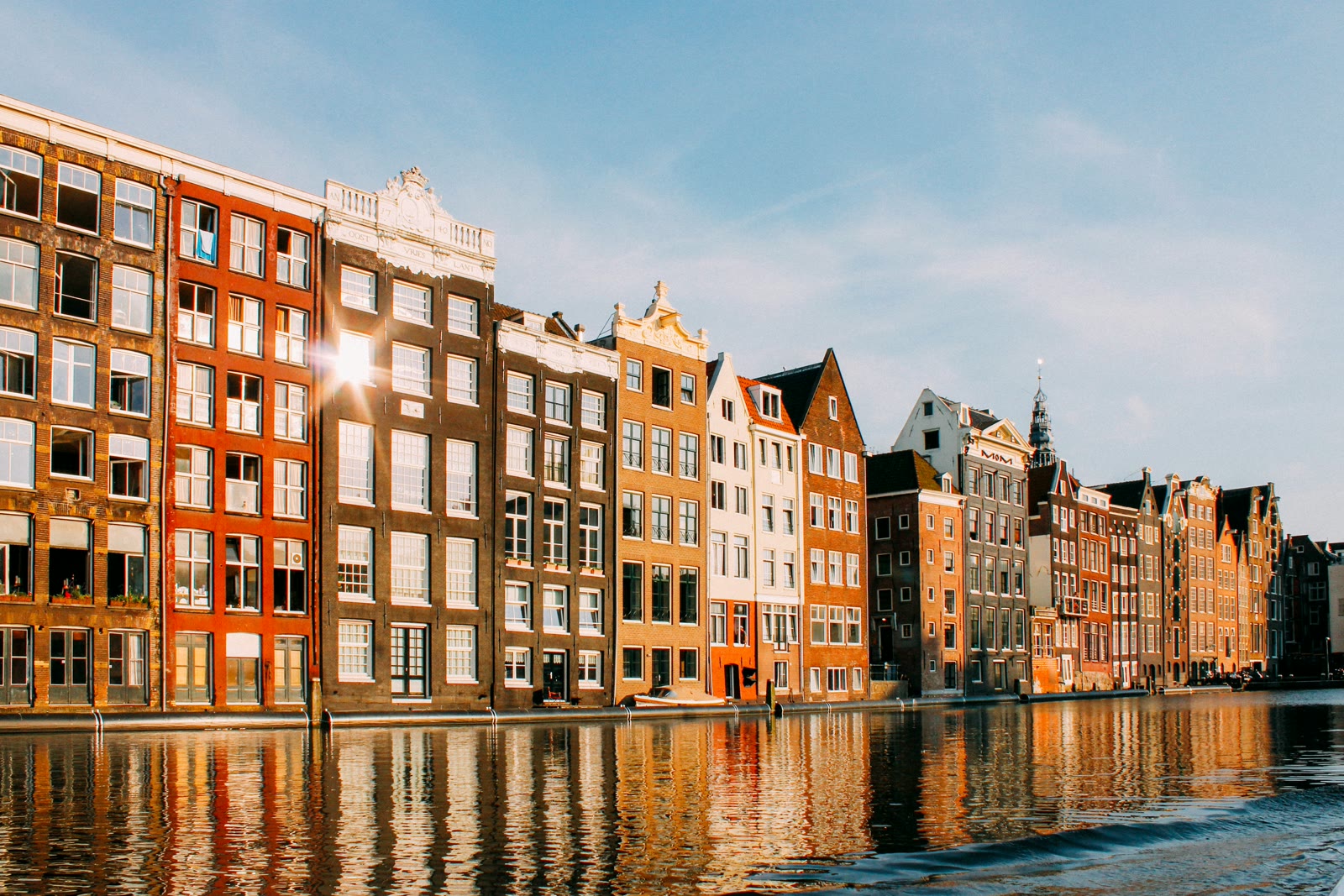 Row of colorful historic canal houses reflected in Amsterdam's calm canal water with trees lining the waterfront