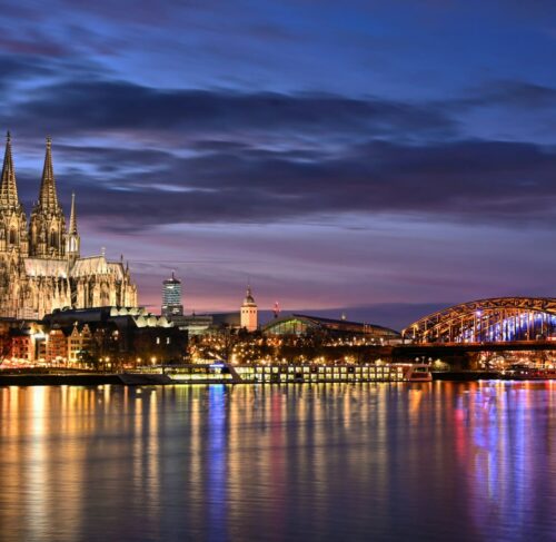 Cologne Cathedral and Hohenzollern Bridge illuminated at night across the Rhine River