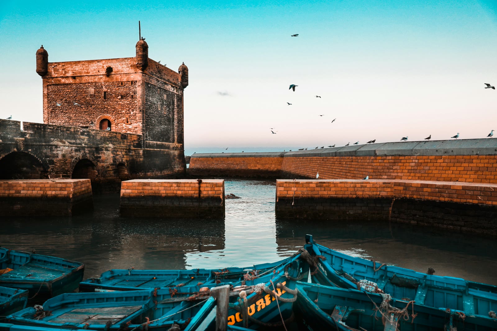 Brown brick buildings near the water in Essaouira Morocco with the fortified port and fishing boats on a clear day