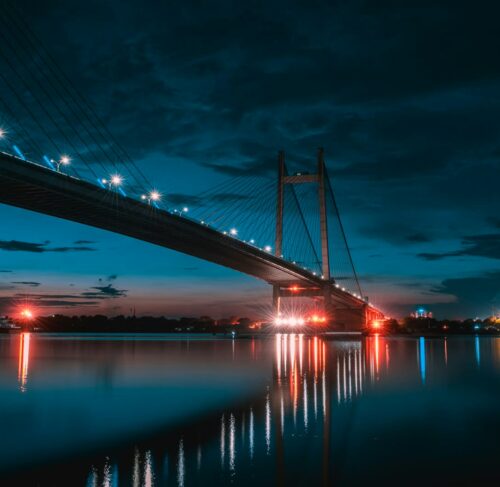 Howrah Bridge illuminated at night over the Hooghly River in Kolkata with city lights reflecting on the water