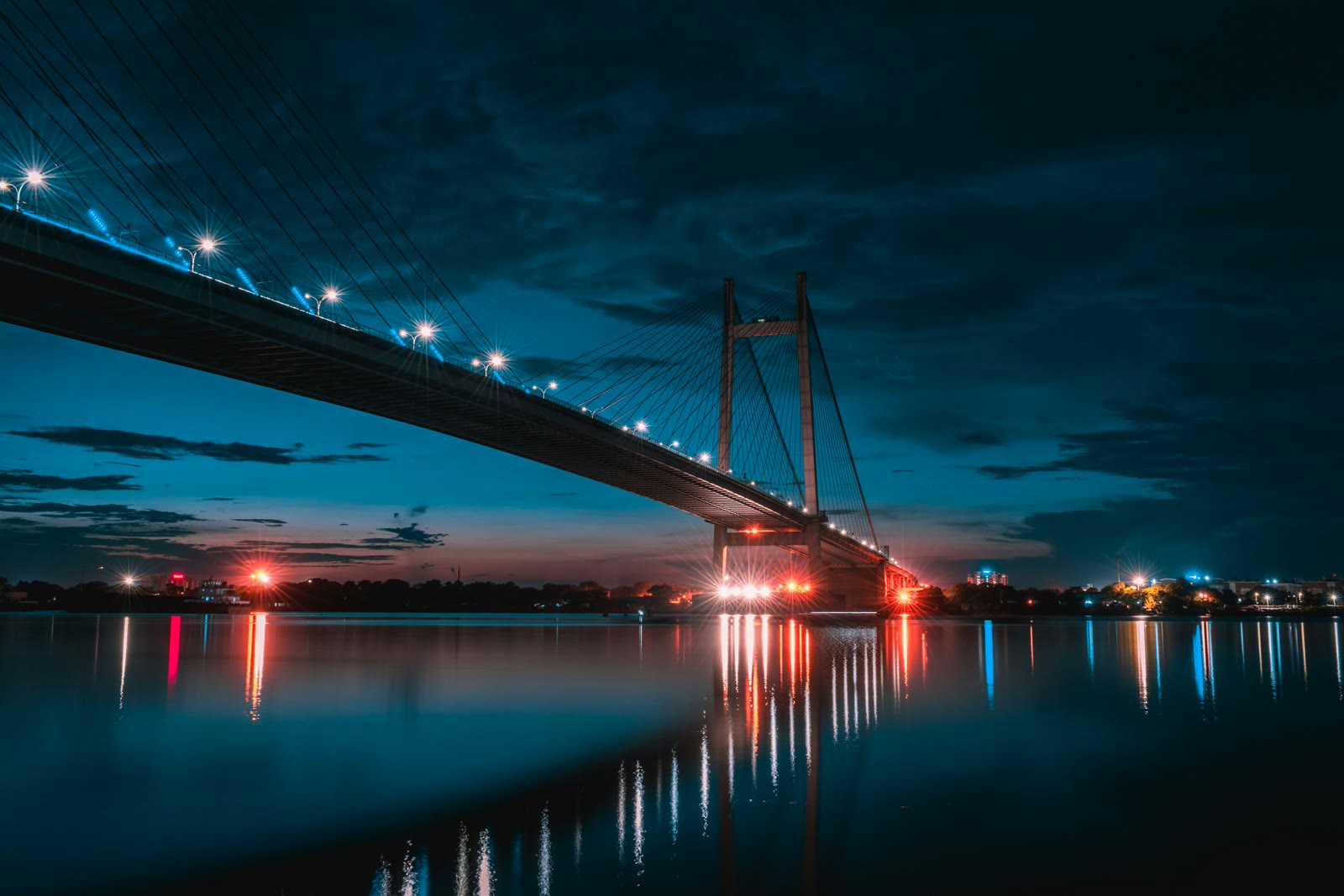 Howrah Bridge illuminated at night over the Hooghly River in Kolkata with city lights reflecting on the water