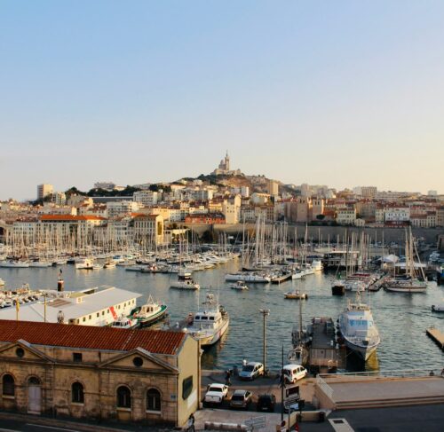 White boats docked at a pier in Marseille harbor with city buildings in the background