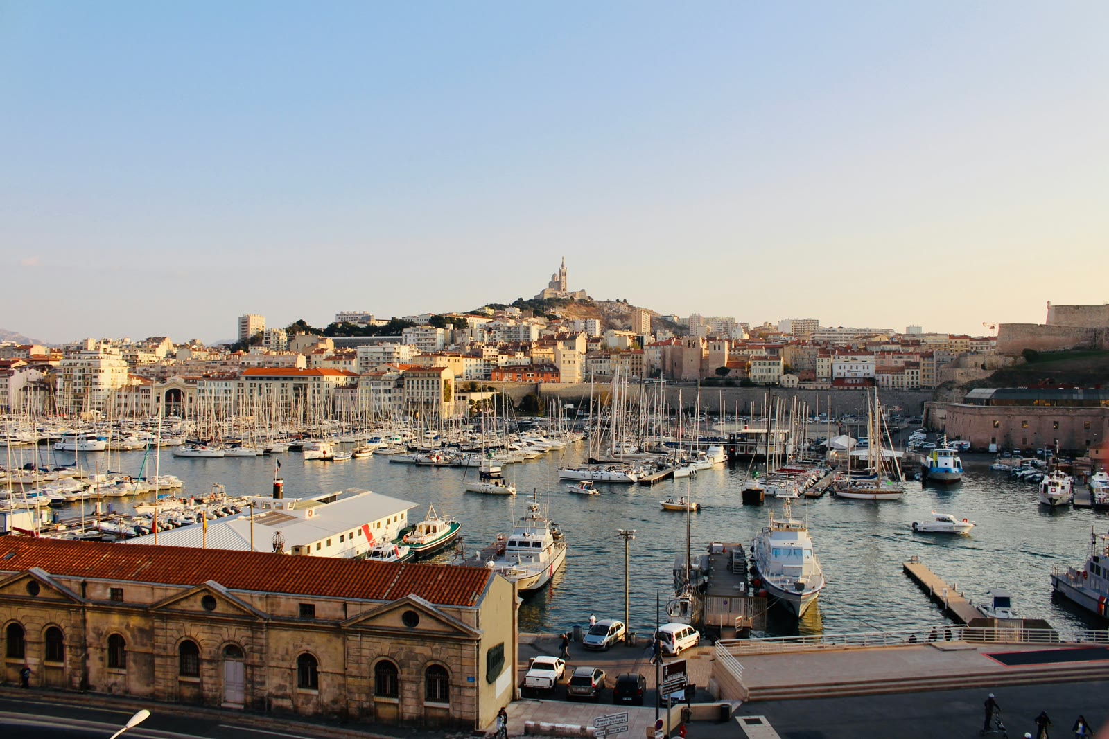 White boats docked at a pier in Marseille harbor with city buildings in the background