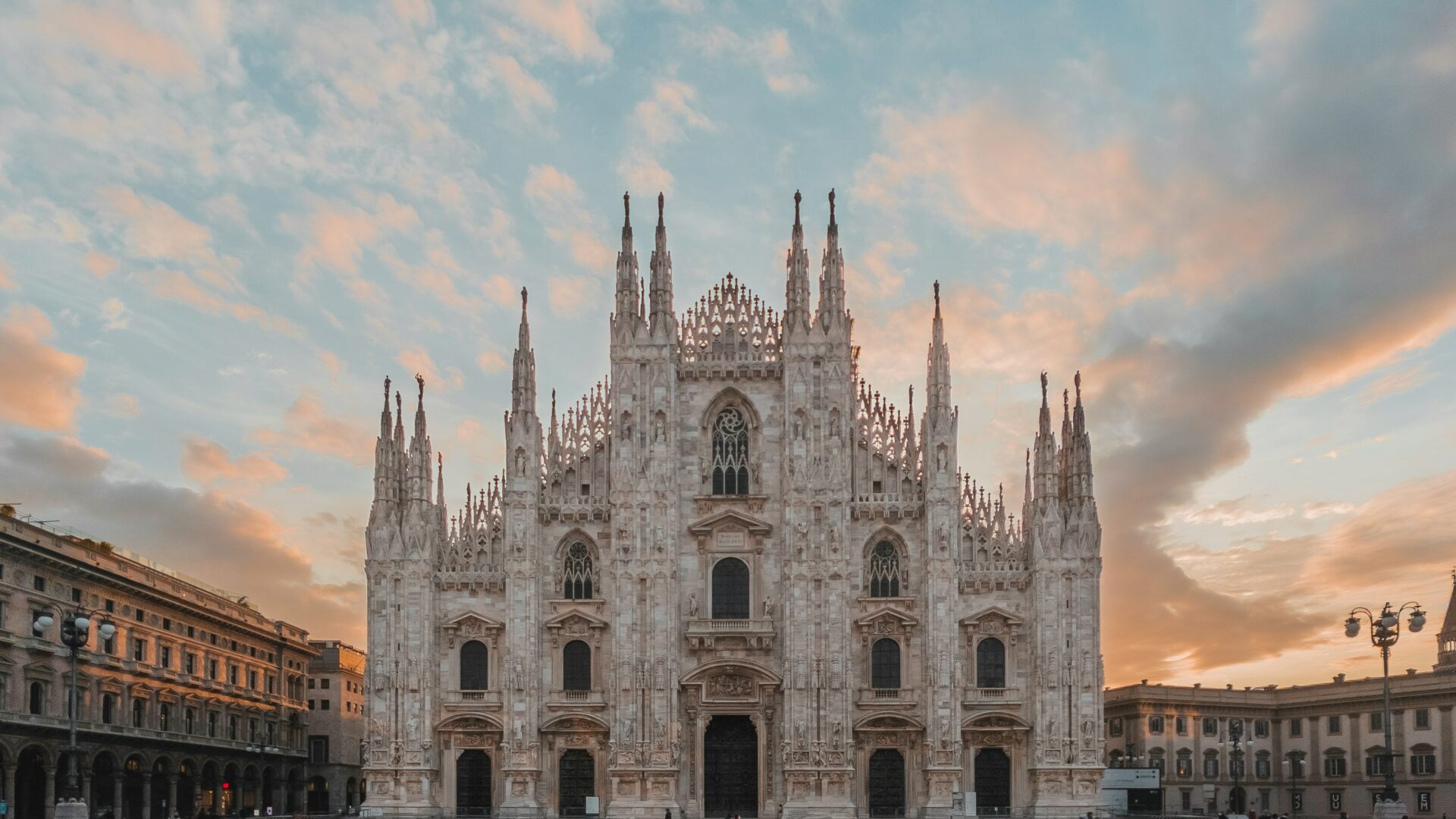 People walking along a sunlit Milan street with historic brown architecture and outdoor cafe seating in the city center