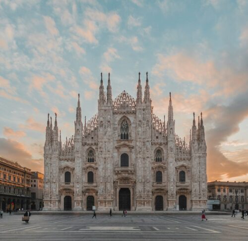 People walking along a sunlit Milan street with historic brown architecture and outdoor cafe seating in the city center