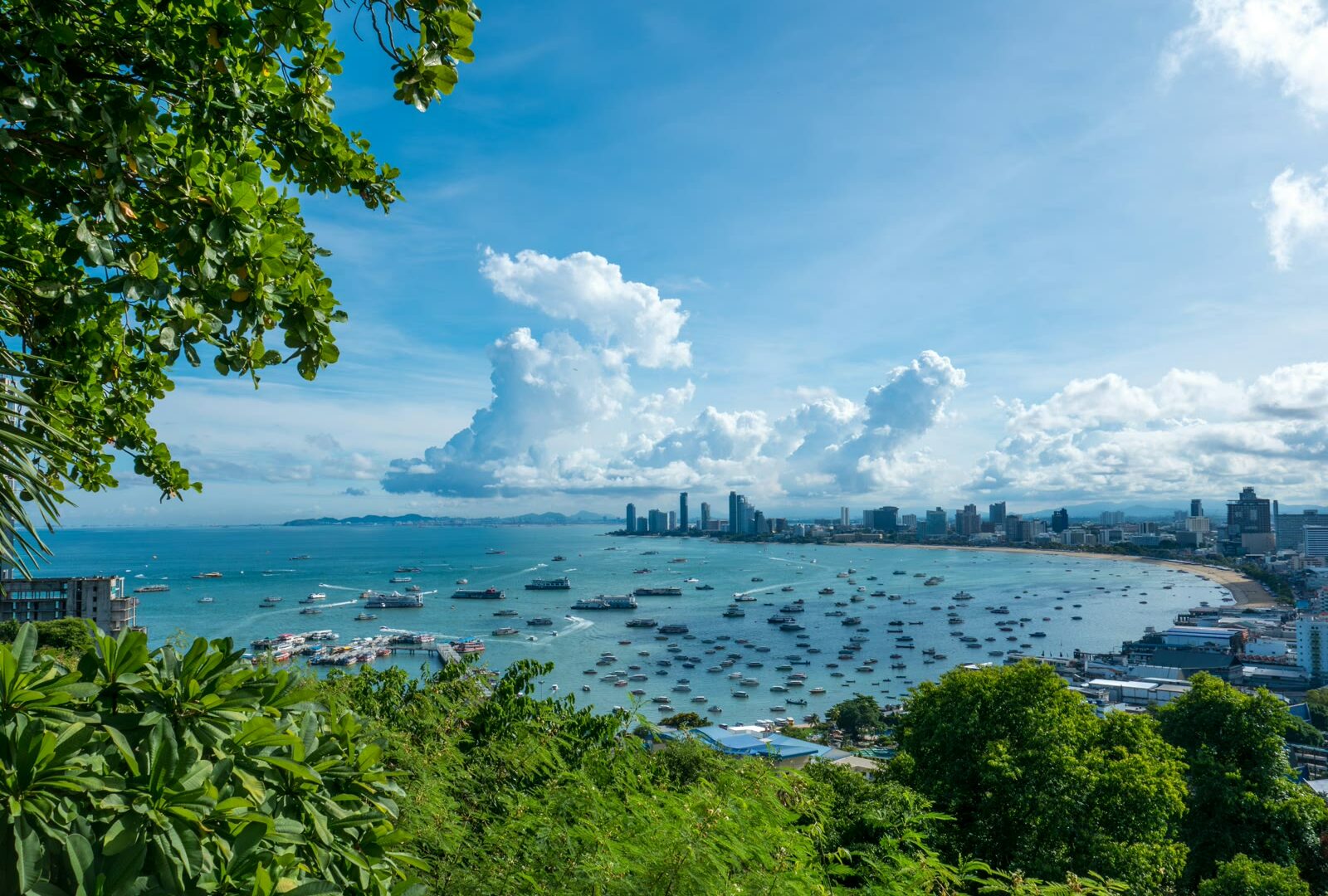 Panoramic view of Pattaya Bay with city skyline, coastline, and calm blue water under partly cloudy sky