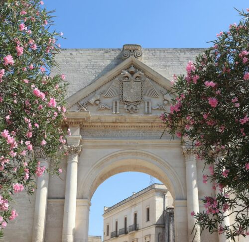 Ancient stone arch framed by pink flowers in Lecce, Apulia, Italy
