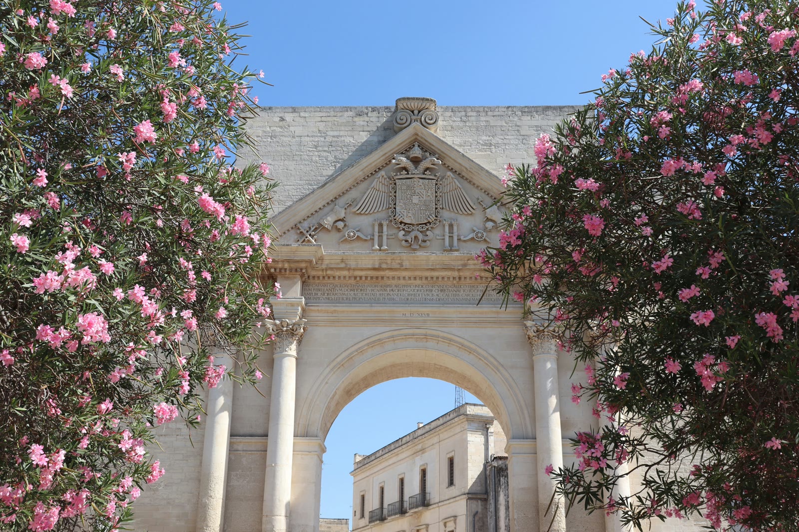 Ancient stone arch framed by pink flowers in Lecce, Apulia, Italy