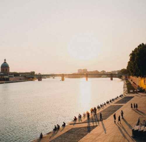 People sitting along the Garonne River near Pont Neuf in Toulouse, Occitanie, France