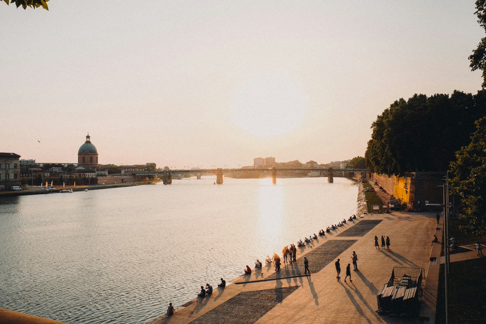 People sitting along the Garonne River near Pont Neuf in Toulouse, Occitanie, France