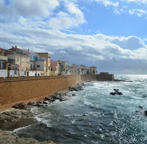 Brown concrete building by the sea under blue sky, Alghero, Sardinia, Italy