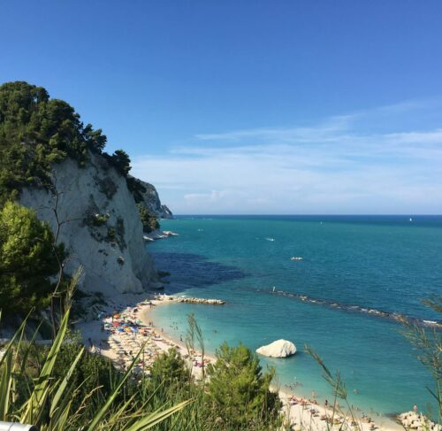 Green and brown rocky mountain alongside blue sea under blue sky, Ancona, Marche, Italy