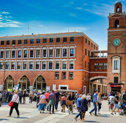 Crowd of people walking around a brick building in Ferrara, Emilia-Romagna, Italy