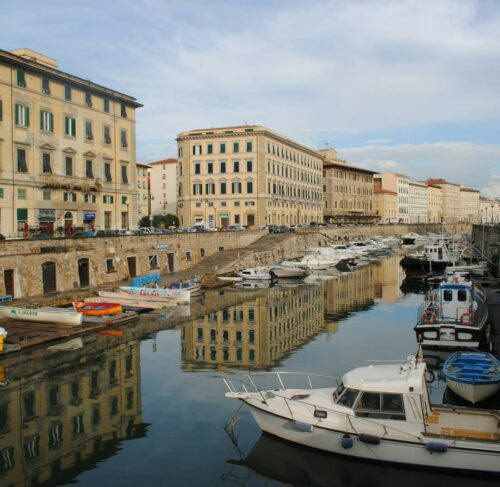 White and blue boat in the water near a brown building in the Venice district, Livorno, Tuscany, Italy