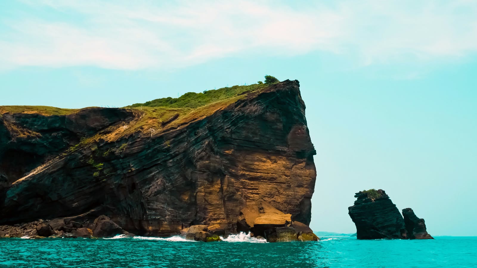 Brown and green rock formation in the sea under white clouds in Veracruz, Mexico
